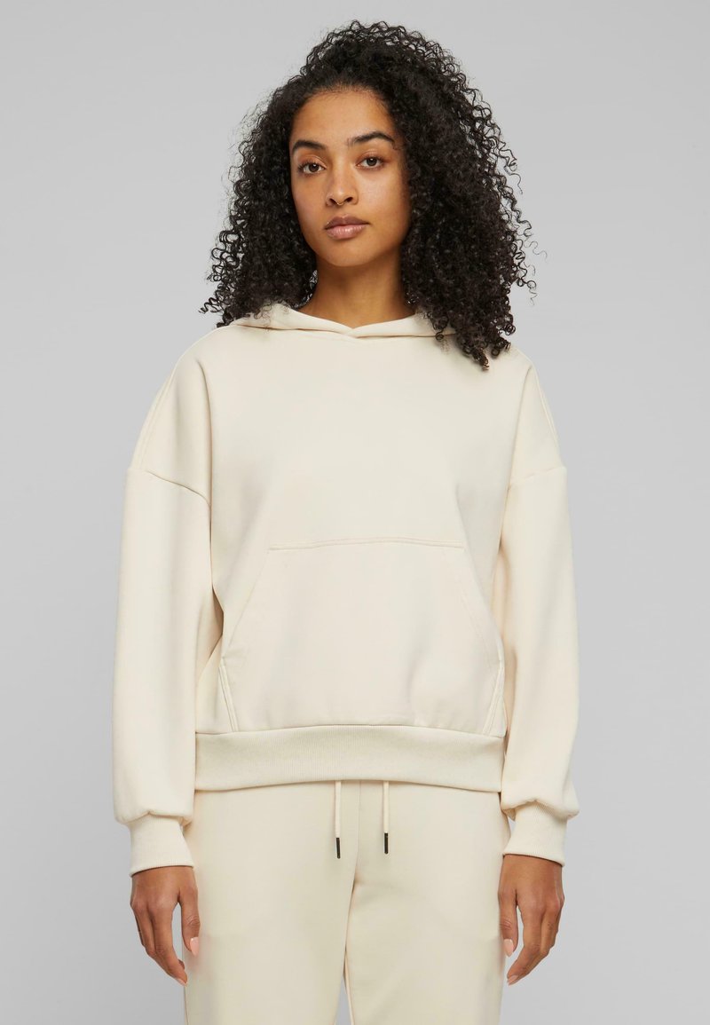 Haut à capuche beige avec une poche avant, un cordon de serrage et des poignets côtelés. Fabriqué en tissu doux, avec une coupe décontractée et une texture lisse.