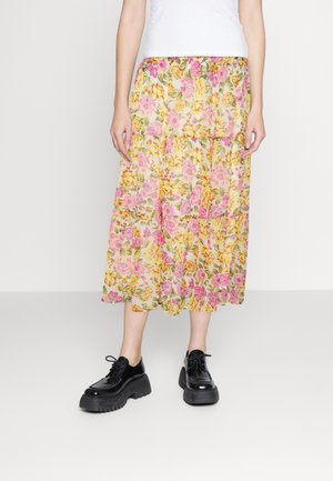 Blumen-Midi-Rock in Gelb mit rosa und grünen Mustern, geraffte Taille und leichte Stoffqualität. Kombiniert mit mattschwarzen Plateauschuhen.