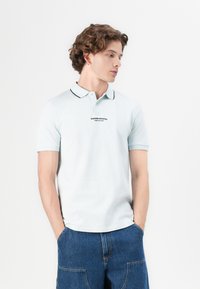 Svetlomodrá polokošele s čiernymi lemami pozdĺž goliera a rukávov. Na hrudi je vyšívané logo. Vyrobená z hladkej bavlnenej zmesi.