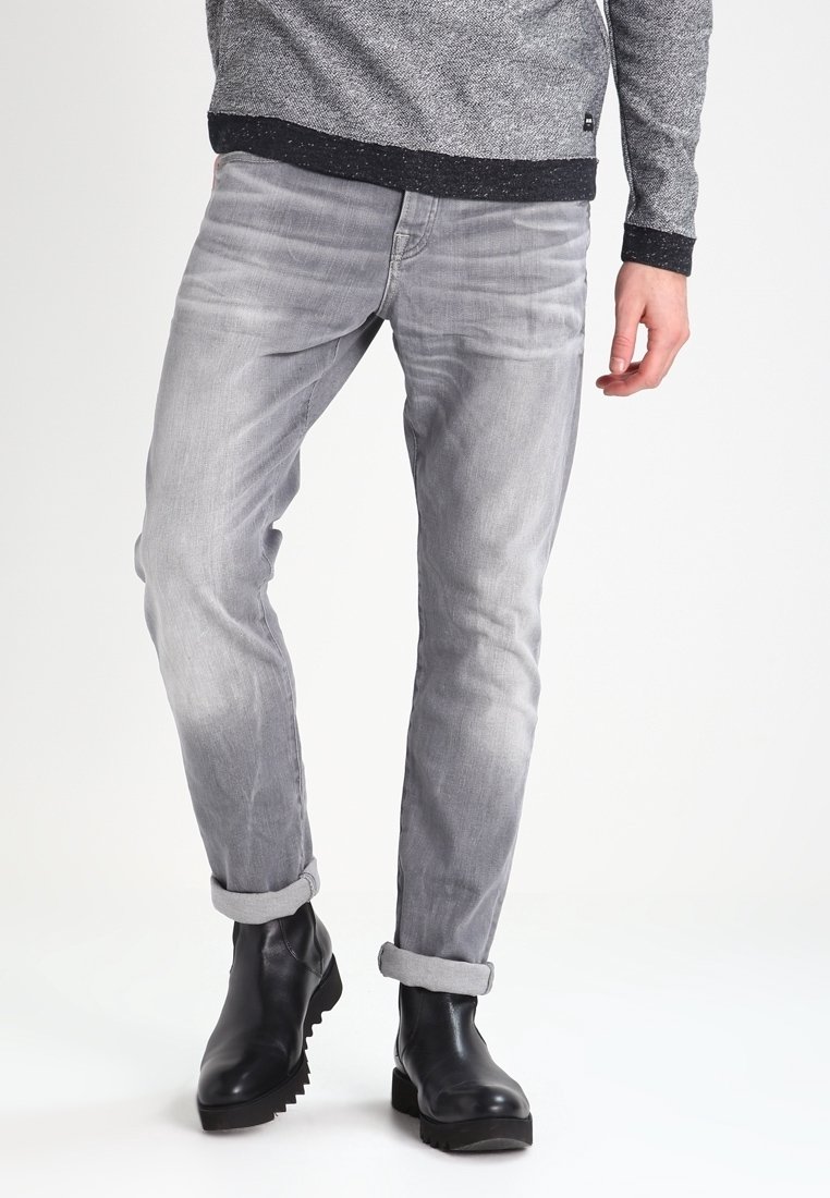 Jean en denim gris avec une coupe slim, présentant une texture délavée et des ourlets retroussés, portés avec des bottines noires.