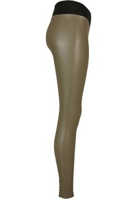 Leggings vert olive avec une large ceinture noire ; fabriquées dans un matériau extensible et brillant ; design ajusté épousant la jambe.