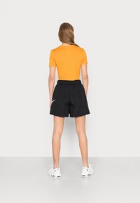 T-shirt fitted arancione a maniche corte, abbinato a pantaloni corti neri a vita elastica con texture e scarpe da ginnastica bianche. Design semplice, senza motivi.