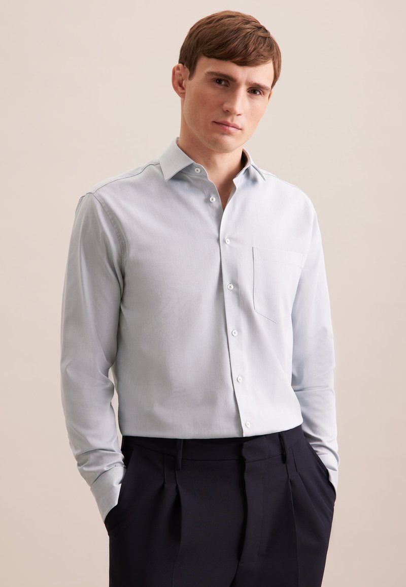 Camicia button-up azzurro chiaro a maniche lunghe con colletto a punta e taschino singolo. Realizzata in tessuto morbido, abbinata a pantaloni scuri.
