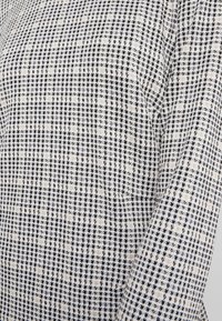 Acercamiento del tejido de patrón de espiga en blanco y negro en una prenda de manga larga con costura visible a lo largo del brazo.