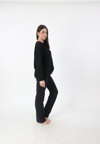 Zwarte gebreide trui met een losse pasvorm, geribbelde boorden, gecombineerd met zwarte rechte jeans en beige sandalen. Effen witte achtergrond.