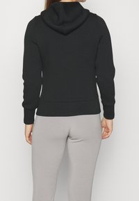 Sweat à capuche noir à coupe décontractée, manches longues et capuche. Fabriqué en tissu doux, avec un ourlet et des poignets côtelés, porté avec un legging gris.