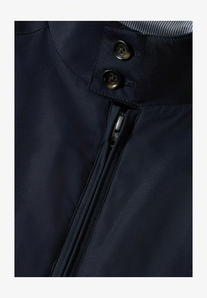 Marineblaue Jacke mit glatter Textur, einem durchgehenden Reißverschluss und zwei runden schwarzen Knöpfen am Kragen. Innenfutter aus gestreiftem Stoff.