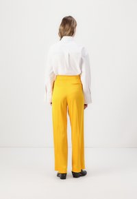 Hvit skjorte med knapper kombinert med gule, høy midje, vide bukser. Sorte hæler fullfører antrekket. Rent, minimalistisk design.