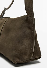 Borsa a tracolla in suede marrone, caratterizzata da una superficie morbida, una forma elegante e dettagli cuciti lungo il lato, con una singola tracolla regolabile.