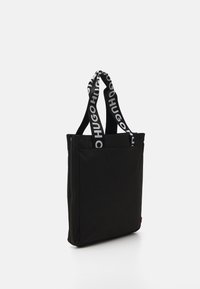 Sac fourre-tout noir en matériau durable, doté de longues anses avec le logo "Hugo", de forme rectangulaire et d'un dessus zippé.