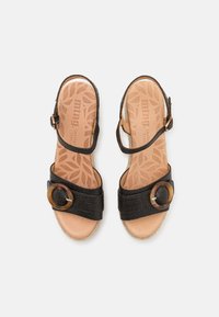 Sandalias de cuero negro con correa ajustable en el tobillo, acento circular marrón y tiras texturizadas; plantilla acolchada de color beige con patrón de hojas.