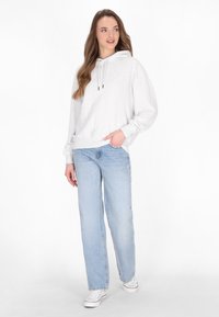 Hanorac gri din bumbac cu buzunar frontal și șnur, purtat cu blugi lejeri bleu deschis și adidași albi. Textură netedă, croi casual.