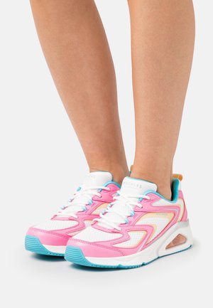 Beny iført hvide mesh-sneakers med pink, blå og orange accenter, tykke såler og synlig luftpolstring på en hvid baggrund.