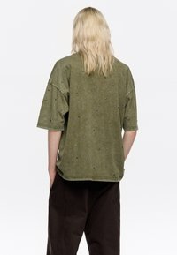 Camiseta verde de manga corta y oversize, con pequeños studs plateados distribuidos uniformemente en la tela. Material de algodón texturizado.