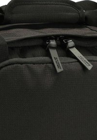 Zaino nero con tessuto testurizzato, doppie cerniere con tiranti neri e un design strutturato. I dettagli includono cuciture rinforzate.