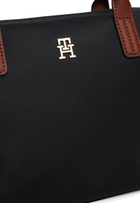 Black nylon handbag with brown leather accents, featuring a gold-tone logo. Structured shape, smooth texture, and dual handles for carrying.