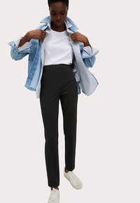 Svarta skräddarsydda byxor med hög midja, kombinerade med en vit t-shirt och en denimjacka. Modellen bär vita sneakers.