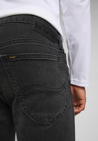 Svart denimjeans med en mjuk textur, med en rundad bakficka och en svart märkesläderlapp vid midjan.
