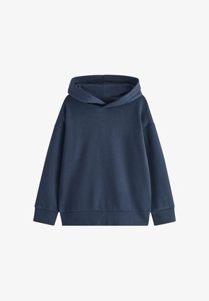 Junger Junge lächelt, trägt einen dunkelblauen Hoodie und passende Hose, darunter lugt ein braun gestreiftes Hemd hervor.