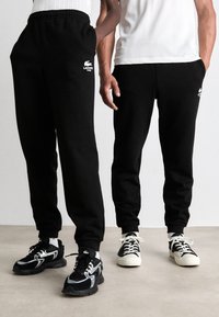 Zwarte sweatpants met elastische tailleband en boorden, voorzien van een geborduurd wit Lacoste-logo. Draag ze met contrasterende zwart-witte sneakers.