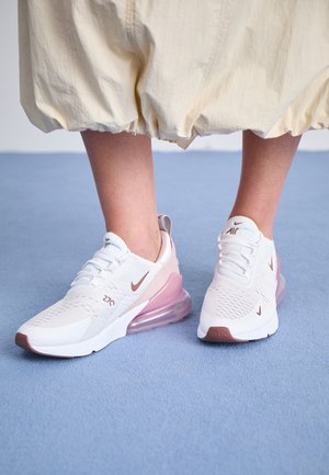 Hvide og lyserøde Nike Air Max 270-sneakers båret med cremefarvede, vide, korte bukser på blåt tæppe.