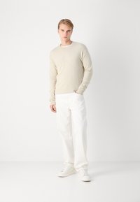 Maglione beige con scollo a costine, abbinato a pantaloni bianchi a gamba dritta e scarpe da ginnastica bianche. Design minimalista e trama morbida.