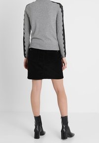 Grå tröja med spetsdetaljer på ärmarna, ihop med en svart kordflods-kjol. Modellen bär svarta ankelstövlar med klack.