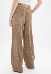 Pantalons en velours côtelé marron à jambe large avec des côtes verticales et une texture douce, dotés d'une taille élastique pour plus de confort et d'une coupe décontractée.