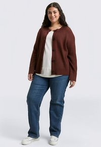 Cardigan côtelé couleur bordeaux, ouvert à l'avant avec un col rond et six boutons. Porté sur un haut blanc et associé à un jean bleu et des baskets blanches.