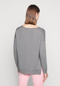 Maglione grigio chiaro dal taglio comodo, con scollatura rotonda e pannelli trasparenti sulle spalle. Il bordo a costine e il dettaglio sul retro aggiungono texture.