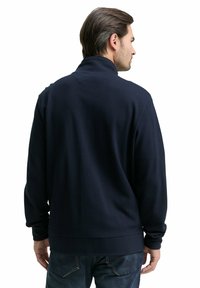 Marineblauwe fleece-pullover met een hoge kraag, gestructureerde stof en geribbelde zoom. Eenvoudig ontwerp, lange mouwen en een losse pasvorm.
