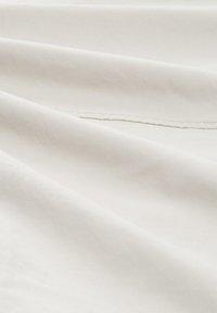 Tejido color crema con una textura suave, que presenta pliegues sutiles y detalles de costura. La superficie parece suave y ligera.