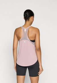 Ανοιχτό ροζ αμάνικη μπλούζα με πλέγμα στην πλάτη, με στρογγυλεμένη βάση και λεπτομέρεια ανακλαστικής κουκκίδας, συνδυασμένη με μαύρο σορτς.