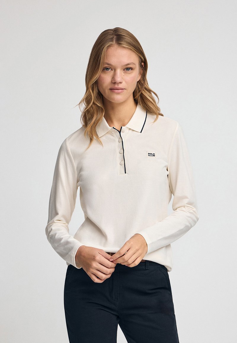 Polo a maniche lunghe in crema, con una chiusura a bottoni, bordino blu sul colletto e un piccolo logo sul lato sinistro del petto. Tessuto morbido.