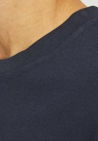 Mørkeblå crewneck sweater med ribbet halsudskæring, lavet af glat stof, der viser en subtil struktur og et nærbillede af det øverste skulderområde.