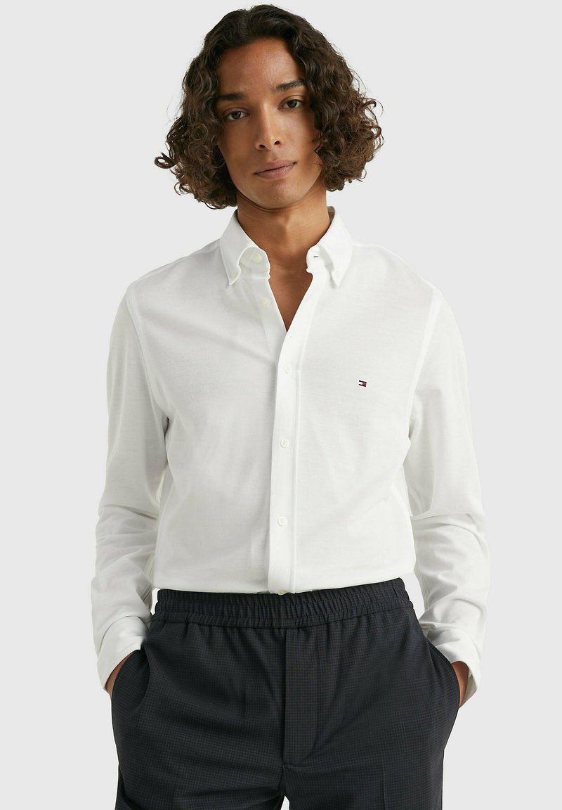 Camicia bianca a maniche lunghe con colletto, dotata di un piccolo logo sul petto. Abbinata a pantaloni navy con vita elastica.