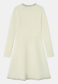 Abito a maniche lunghe in crema chiaro, con texture a coste nella parte superiore e tessuto liscio sotto, caratterizzato da un orlo decorato con logo.