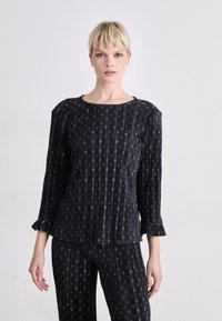 Schwarzes, gemustertes Oberteil mit Dreiviertelärmeln, einem runden Halsausschnitt und gerafften Ärmelenden. Der Stoff weist vertikale Linien mit kleinen, kreisförmigen Mustern auf.
