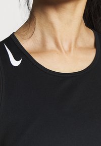 Mustan urheilullinen toppi, jossa on pyöreä kaula-aukko ja valkoinen logoyksityiskohta vasemmalla olkapäällä. Silkkinen, joustava kankaan rakenne.