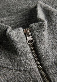 Maglione grigio con collo zip, caratterizzato da un materiale a maglia testurizzata, chiusura frontale con zip e un design casual con una sensazione morbida e pelosa.