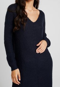 Marinblått stickat klänning med v-ringning och långa ärmar, med ribbad struktur och avslappnad passform. Utsmyckad med subtila vertikala linjer.