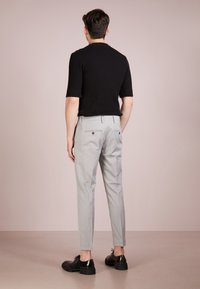 Black ribbed short-sleeved shirt paired with light gray checkered trousers, featuring a fitted style and black shoes with studded accents.