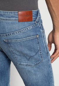 Ljusblå denimjeans med detaljer på bakfickorna, läderlogotyp och synlig sömnad. Har en kroppsnära design och texturerad tyg.