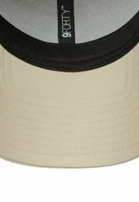 Beige Kappe mit schwarzem Schirm; aus strukturiertem Stoff gefertigt und mit einem Innenschild, das "9FORTY" liest. Das Design ist strukturiert und rund.