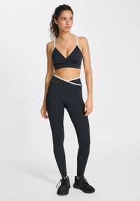 Svart sport-bh med vita band och ett omslag i designen. Svarta leggings med korsmönstrat midjeband och ankellång modell.