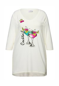 Tunic bianco in cotone con scollo a V, caratterizzato da grafiche di bicchieri da cocktail colorati. Include ciliegie decorative e la parola "Cocktail" in nero.