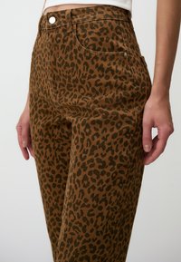 Pantalons en coton imprimé léopard aux teintes brunes avec une coupe ajustée. Comprend des poches avant et un léger éclat sur un tissu texturé.