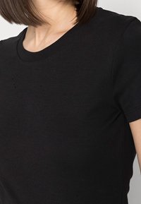 Černé tričko v přiléhavém střihu s krátkými rukávy a kulatým výstřihem. Hladký povrch s viditelným šitím a nepatrnými známkami opotřebení.