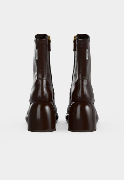 Paire de bottines en cuir marron foncé avec talons épais et tirettes zippées marquées visibles, vue de dos.
