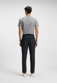 Grå kortärmad t-shirt, m�örka randiga byxor och vita sneakers. Byxorna har en skräddarsydd passform med ett smalrandigt mönster och fickor.
